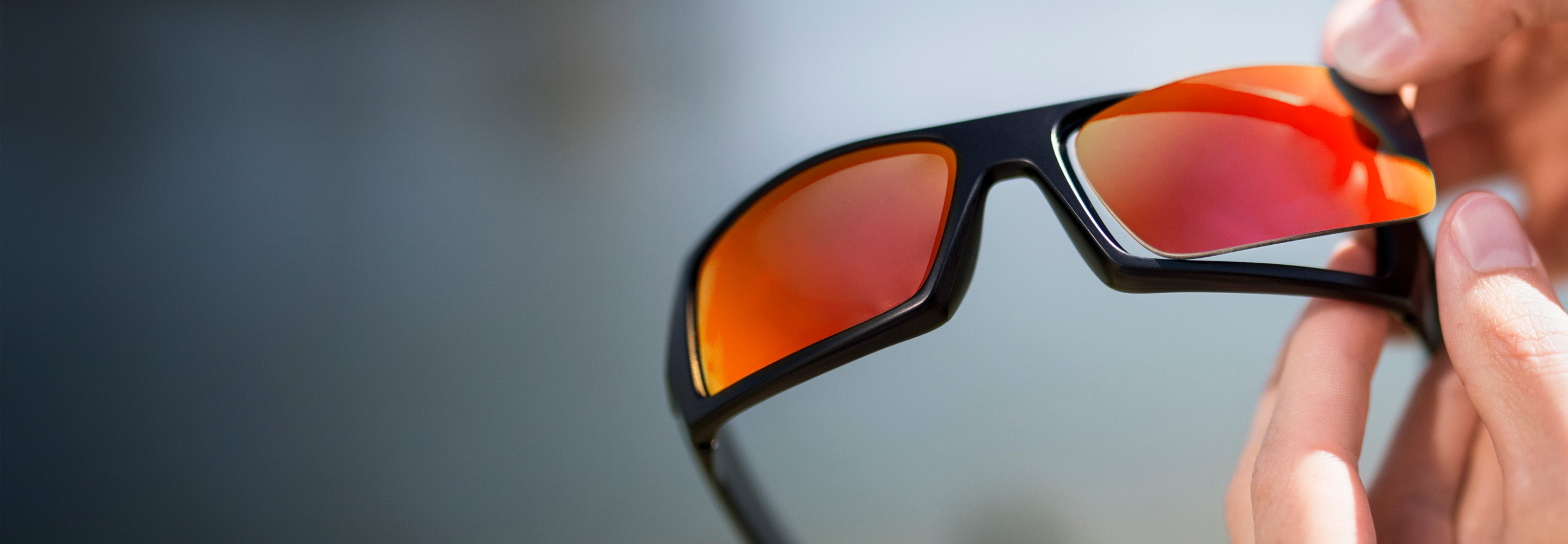 A close-up of hands swapping the orange lenses on black framed sunglasses.
